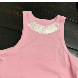 Pink ribbed tank top featuring a neckline detail made from overlapping iridescent shell discs, styled flat on a dark wood background.