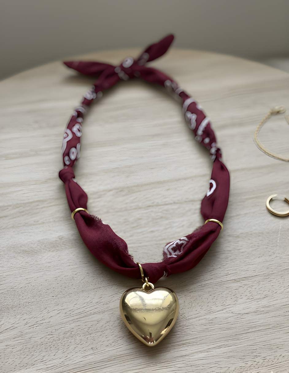 Gold heart charm necklace with burgundy bandana strap on wooden surface